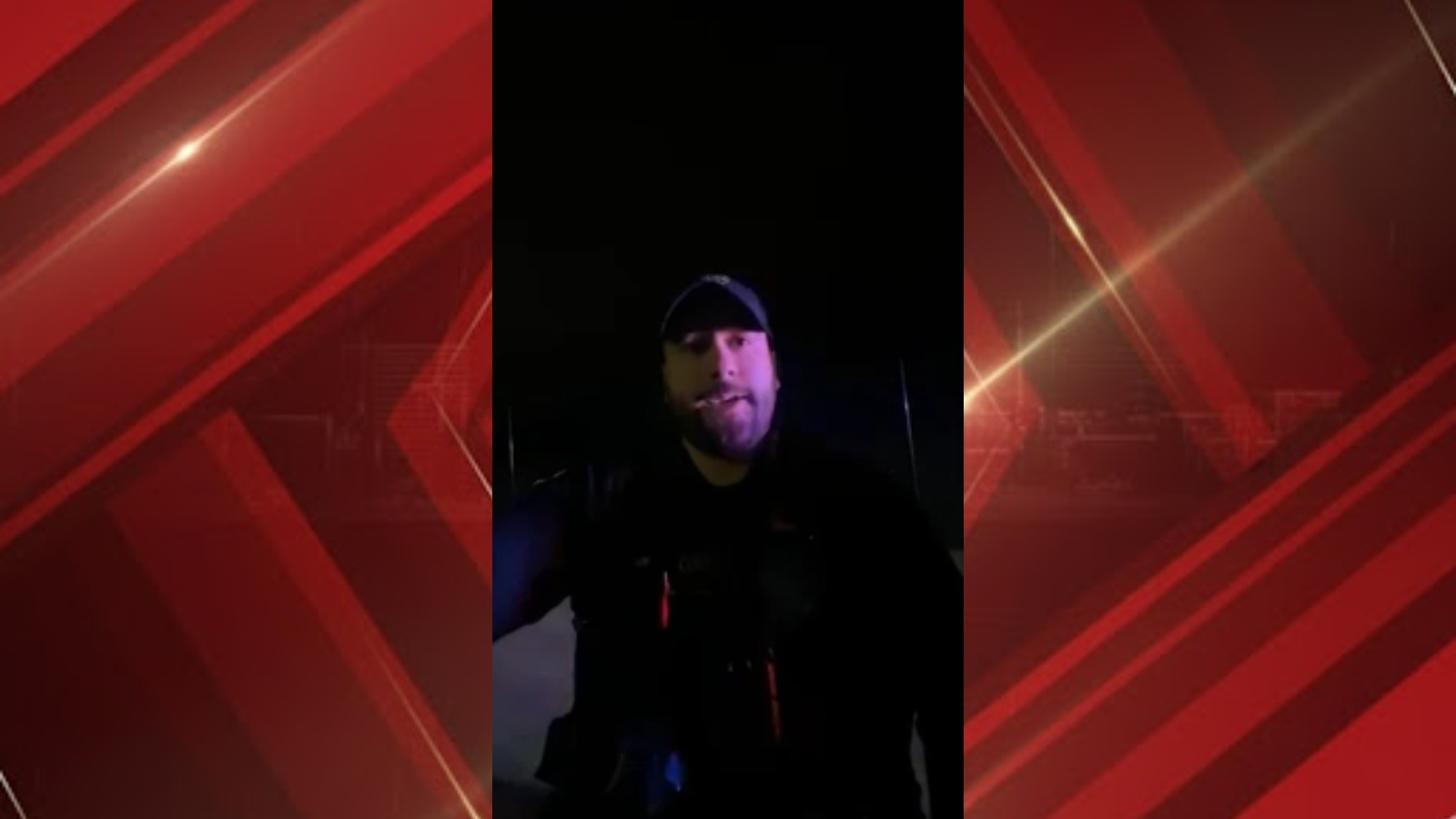 Video still of a man in a cap speaking to the camera at night, dark background.