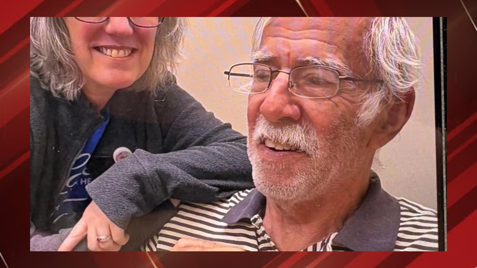 Smiling elderly man with glasses and white hair beside a woman with gray hair in a casual setting.