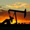 Silhouette of an oil pumpjack against a orange sunset sky.