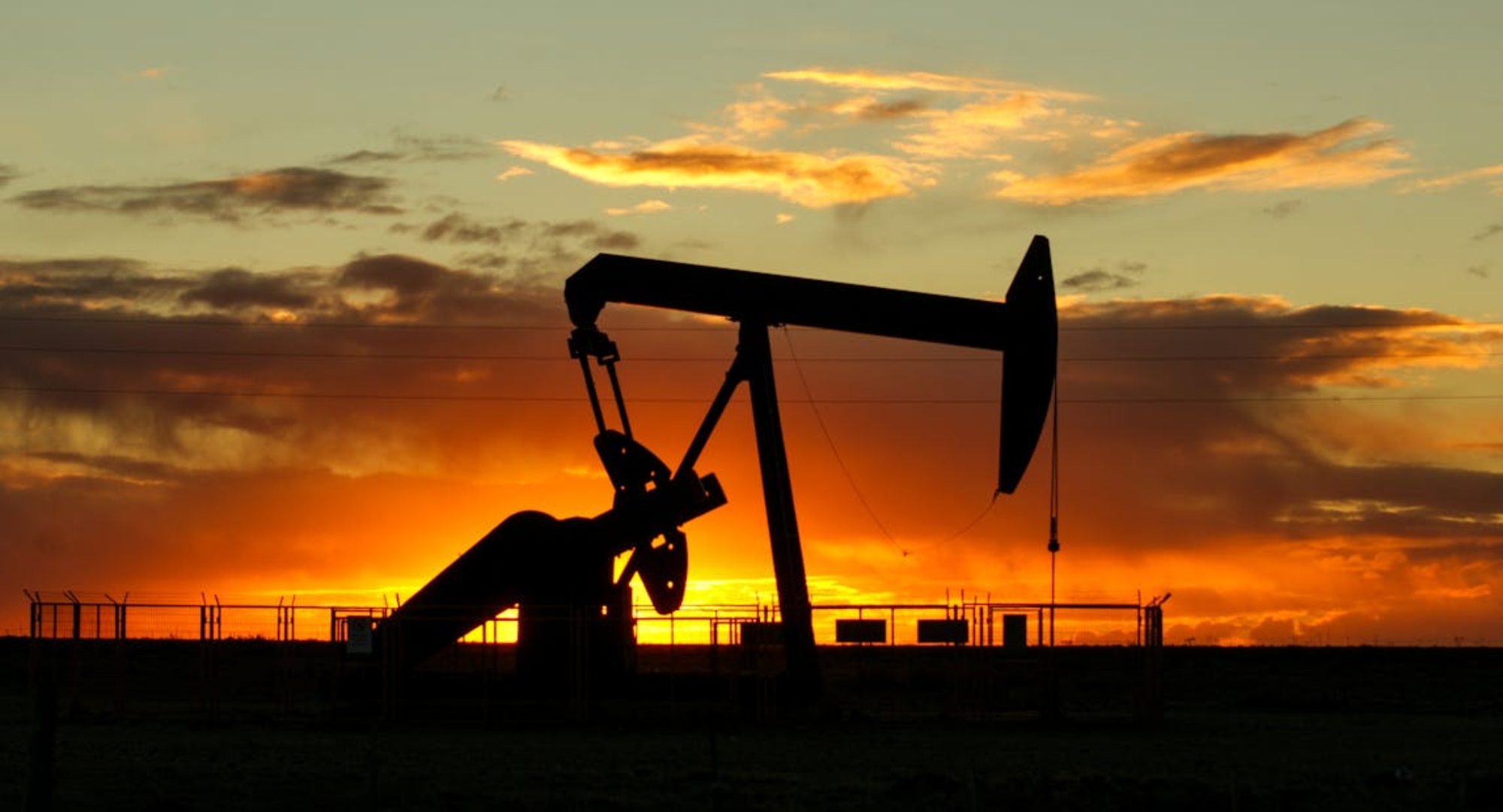 Silhouette of an oil pumpjack against a orange sunset sky.