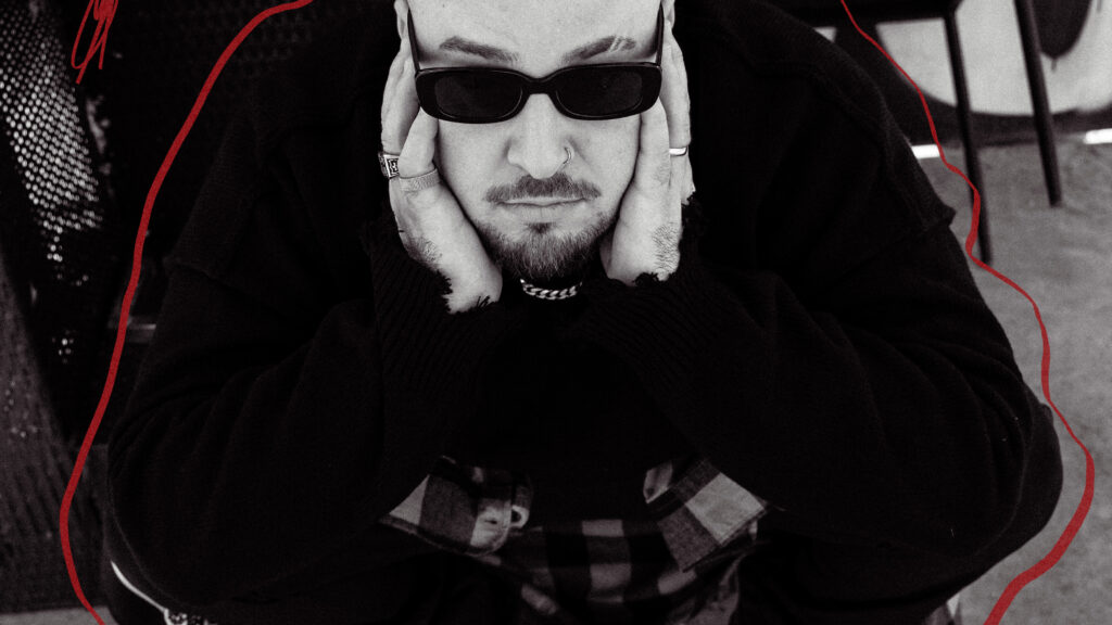 Moody black-and-white portrait of a man wearing sunglasses, with hands cupping his face and head bowed slightly.