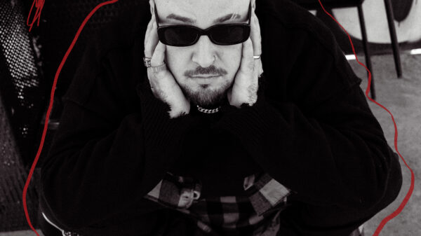 Moody black-and-white portrait of a man wearing sunglasses, with hands cupping his face and head bowed slightly.