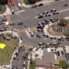 Aerial view of a busy intersection with many police cars and a police presence, plus people gathered in a park with yellow and green tents nearby.