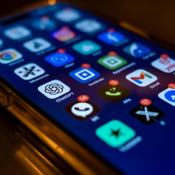 Close-up of a smartphone screen in low light showing glowing app icons on the home screen (Chrome, Gmail, ChatGPT, Messages, etc.).