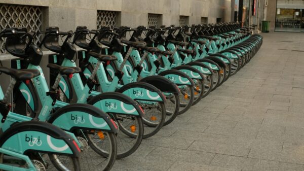 Row of turquoise Bizî bike-sharing bicycles lined up along a city sidewalk near a stone building façade.