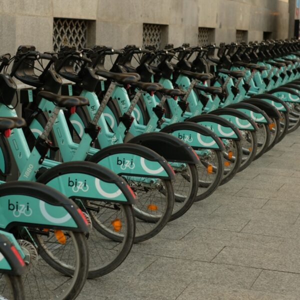 Row of turquoise Bizî bike-sharing bicycles lined up along a city sidewalk near a stone building façade.