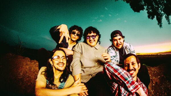 Group of friends posing closely for a selfie outdoors at sunset, smiling and making playful gestures toward the camera.