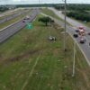 Aerial view of a divided highway with a silver car off the right-side median and emergency crews on the right, securing the scene.