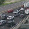 Heavy traffic on a multi-lane highway with cars and trucks lined up in each direction, separated by a concrete barrier and an overpass on the right.