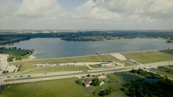 Aerial view of a large lake with a grassy shoreline, park areas, and a road along the edge.