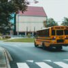 Yellow school bus driving on a curved city street with a crosswalk in the foreground.