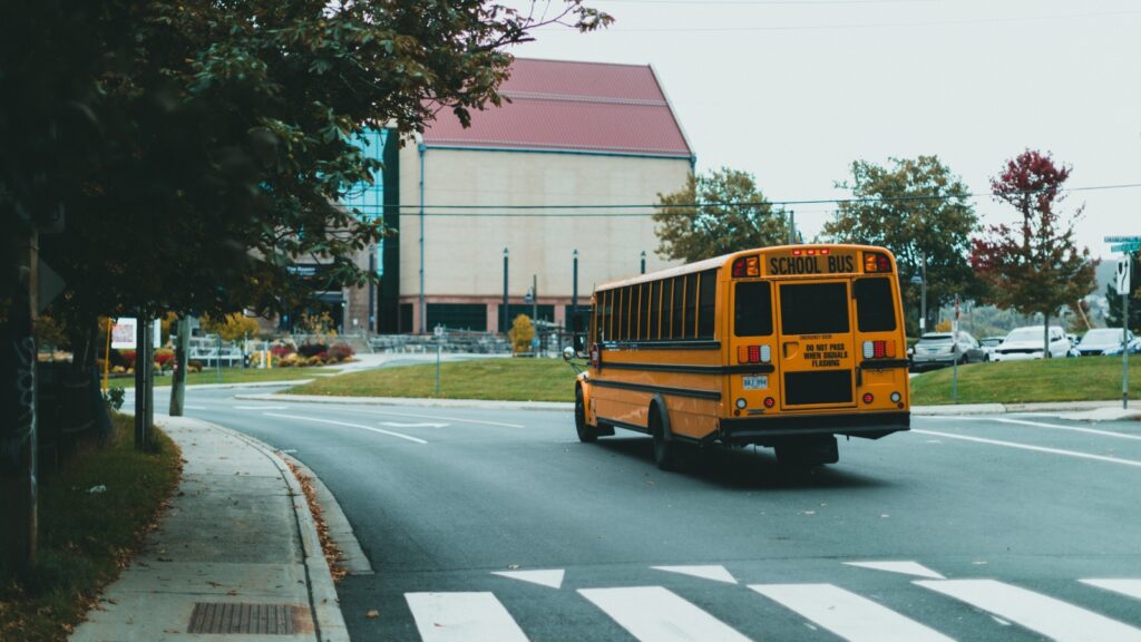 Yellow school bus driving on a curved city street with a crosswalk in the foreground.