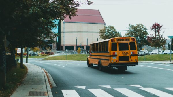 Yellow school bus driving on a curved city street with a crosswalk in the foreground.