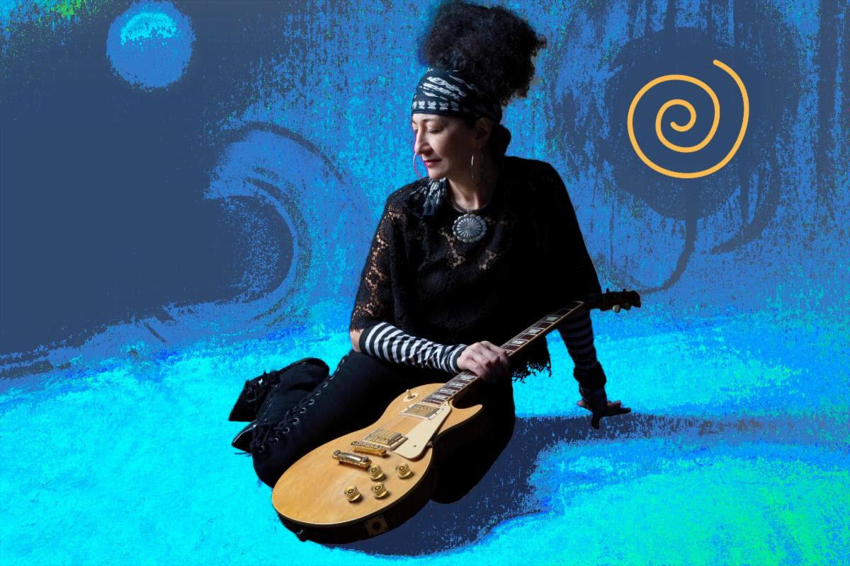 Musician sitting with a gold electric guitar against a blue abstract background with an orange spiral logo on the right.