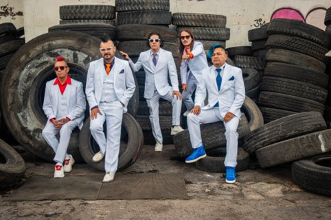 Five people in light-blue suits with colorful ties posing among stacked tires in a junkyard.