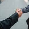 Two businesspeople shaking hands in a professional agreement on a sidewalk backdrop.