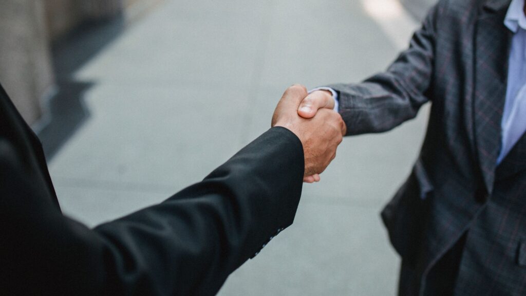 Two businesspeople shaking hands in a professional agreement on a sidewalk backdrop.