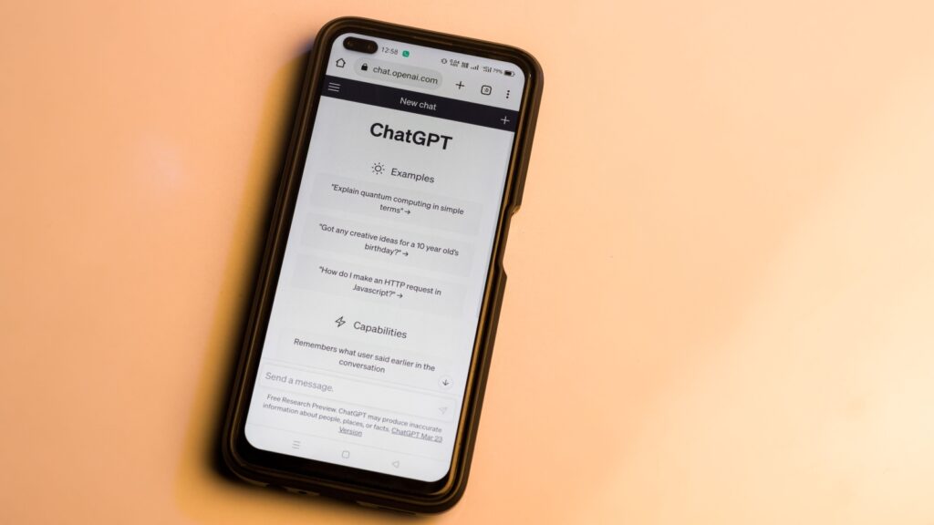 Phone screen showing ChatGPT interface with Examples and Capabilities sections open on a peach background