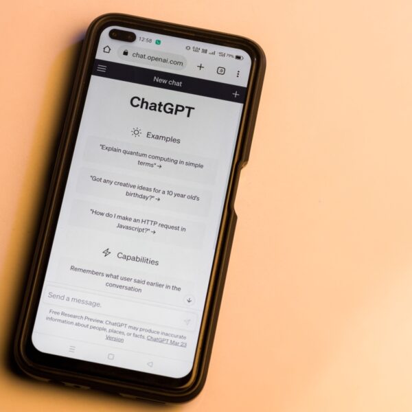 Phone screen showing ChatGPT interface with Examples and Capabilities sections open on a peach background