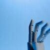 Robotic hand reaching upward against a clear blue sky.