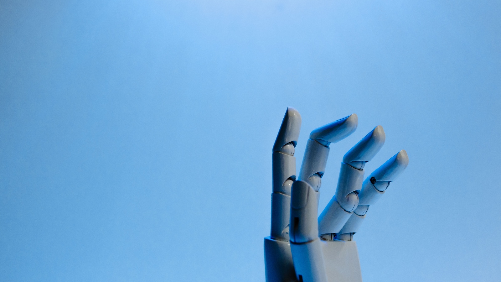 Robotic hand reaching upward against a clear blue sky.