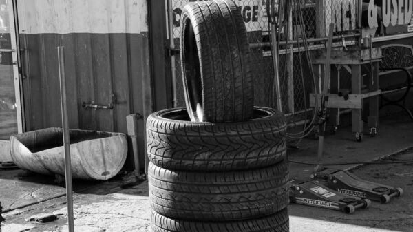 Stack of four car tires outside a repair shop, with one tire leaned upright on top; jack stands and tools nearby.