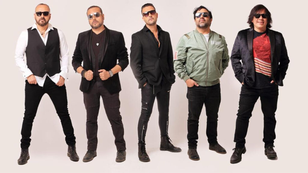 Five men wearing sunglasses pose in a studio, dressed in black jackets and casual outfits, lined up side by side.