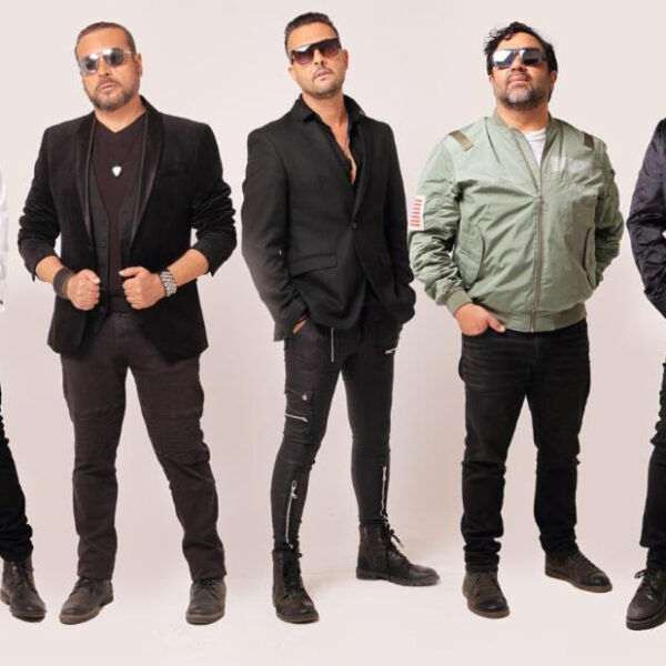 Five men wearing sunglasses pose in a studio, dressed in black jackets and casual outfits, lined up side by side.