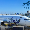 Alaska Airlines Boeing 737 parked at gate 26 with a jet bridge, on the tarmac under a clear blue sky.