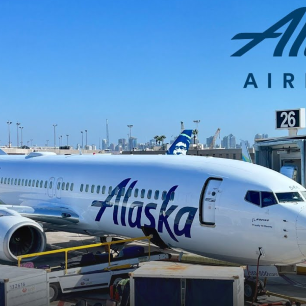 Alaska Airlines Boeing 737 parked at gate 26 with a jet bridge, on the tarmac under a clear blue sky.