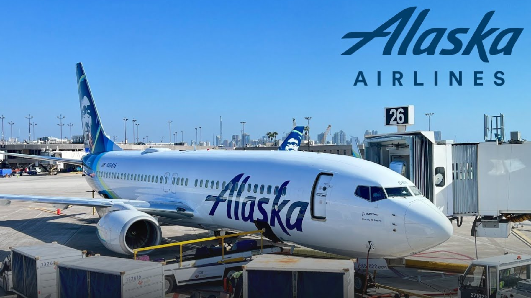 Alaska Airlines Boeing 737 parked at gate 26 with a jet bridge, on the tarmac under a clear blue sky.