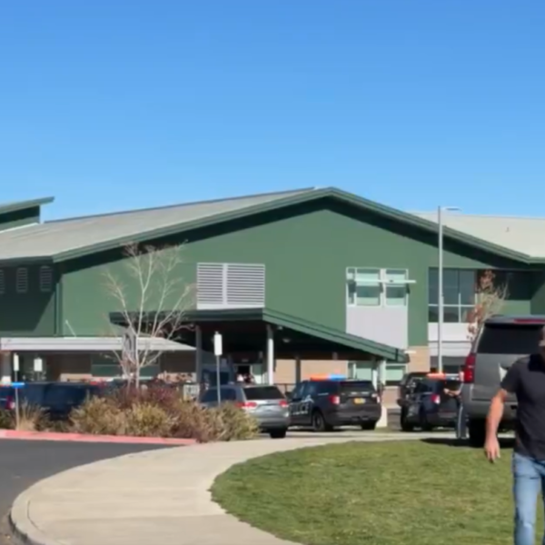 Green building with a sloped roof and parked cars, emergency responders visible outside on a sunny day.