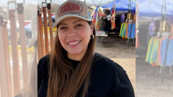 Smiling woman wearing a Texas cap at an outdoor market with colorful clothing stalls in the background.