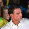 Three men in a crowd: foreground man in a white dress shirt, flanked by a man in a yellow Brazil jersey and a man in black on the right, all looking in the same direction.