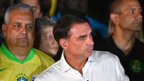 Three men in a crowd: foreground man in a white dress shirt, flanked by a man in a yellow Brazil jersey and a man in black on the right, all looking in the same direction.