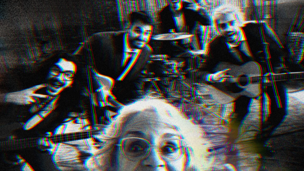 Older woman in front taking a selfie with a four‑piece band in a rehearsal space, features guitar, violin, and drums; image has a red/blue glitch effect.