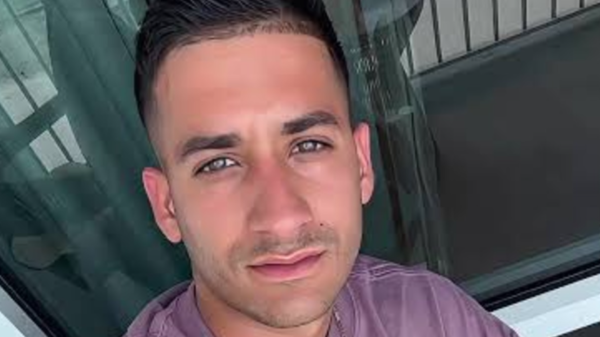 Close-up selfie of a man with short dark hair wearing a mauve shirt, looking at the camera.
