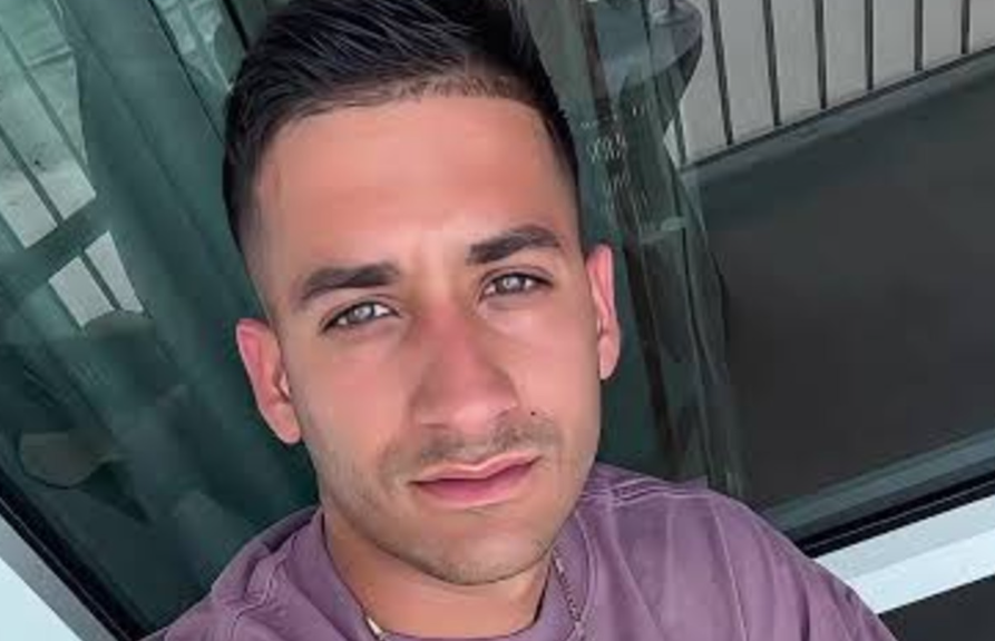 Close-up selfie of a man with short dark hair wearing a mauve shirt, looking at the camera.