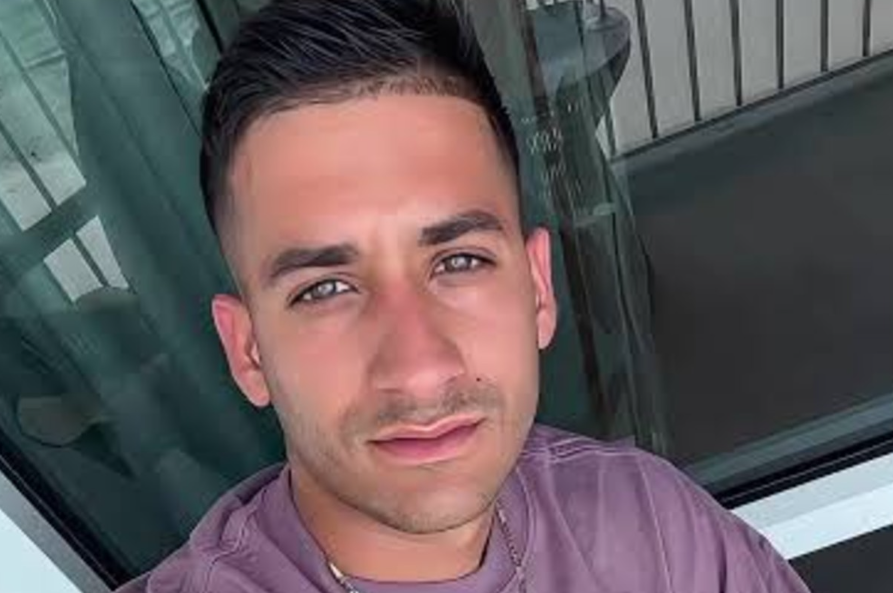 Close-up selfie of a man with short dark hair wearing a mauve shirt, looking at the camera.