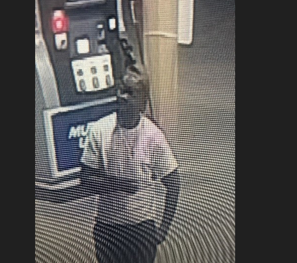 Grainy security cam image of a person in a light shirt and dark pants standing near equipment.