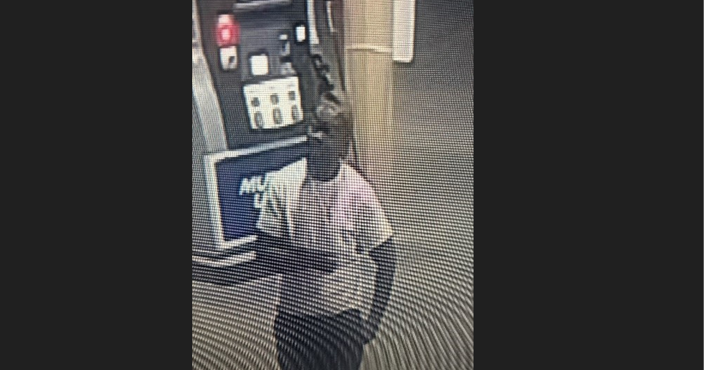 Grainy security cam image of a person in a light shirt and dark pants standing near equipment.
