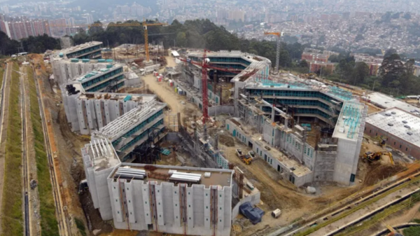 Aerial view of a large construction site with multiple connected concrete buildings, cranes, and construction equipment across a cleared site near a city edge.