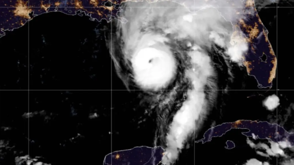 Infrared satellite image showing a tropical cyclone with a well-defined eye near the Gulf of Mexico, approaching the Florida coast with spiral rainbands over dark ocean waters and city lights along the coast visible at night.