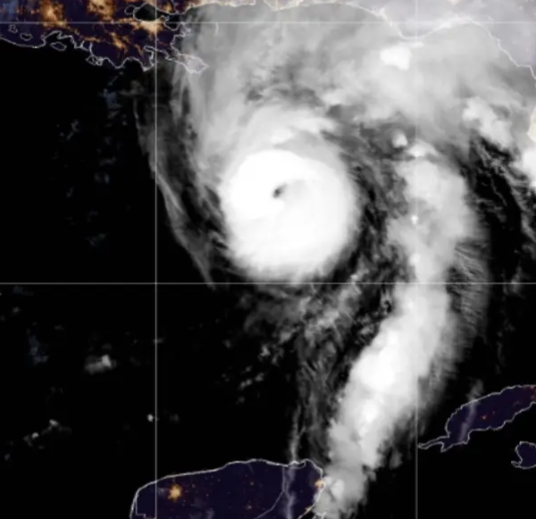 Infrared satellite image showing a tropical cyclone with a well-defined eye near the Gulf of Mexico, approaching the Florida coast with spiral rainbands over dark ocean waters and city lights along the coast visible at night.