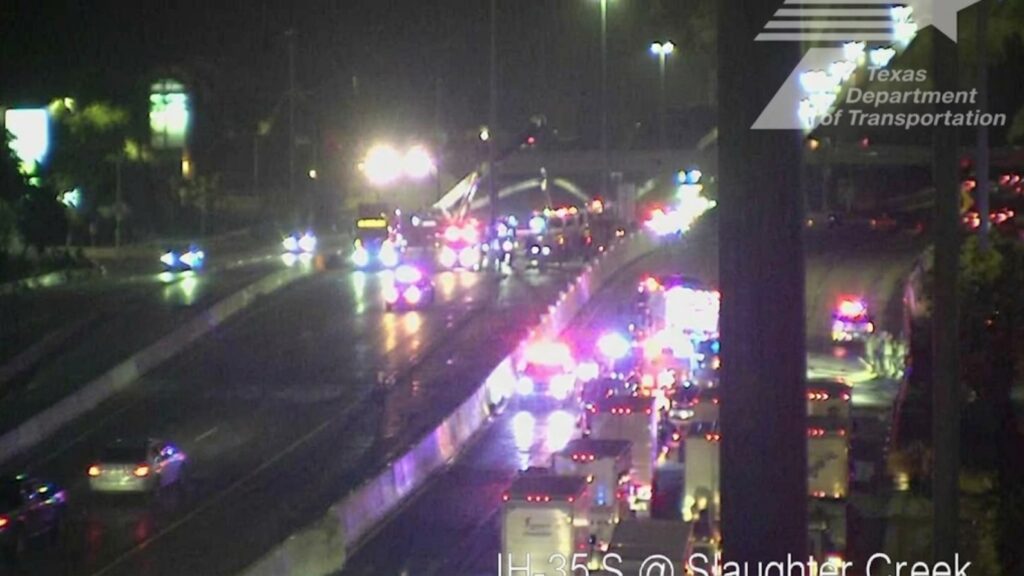 Nighttime highway incident with numerous emergency vehicles and flashing red/blue lights on IH-35 South near Slaughter Creek (TxDOT watermark).