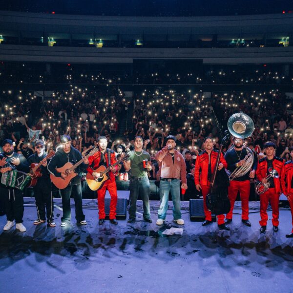 Band and brass section perform on stage in front of a cheering crowd holding up illuminated phones at night concert venue.