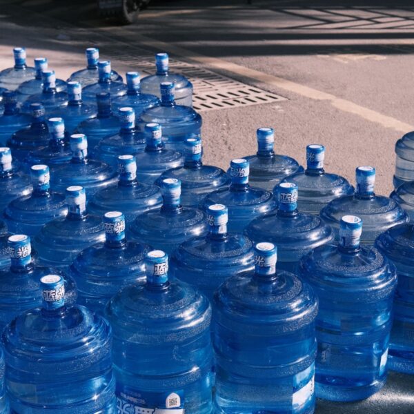 Row of large blue water jugs lined up outdoors, likely for water distribution or emergency supply.