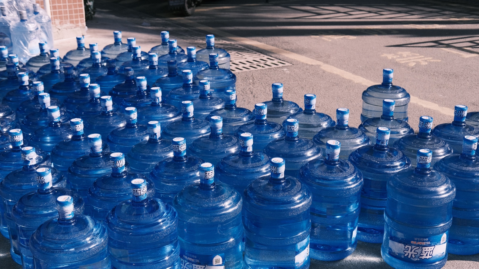 Row of large blue water jugs lined up outdoors, likely for water distribution or emergency supply.