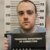 Mugshot portrait of a man in a gray shirt in front of a height measurement board, holding a Tennessee Department of Correction sign below.