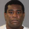 Mugshot of a Black man with short black hair wearing a white shirt against a gray backdrop with a neutral expression.
